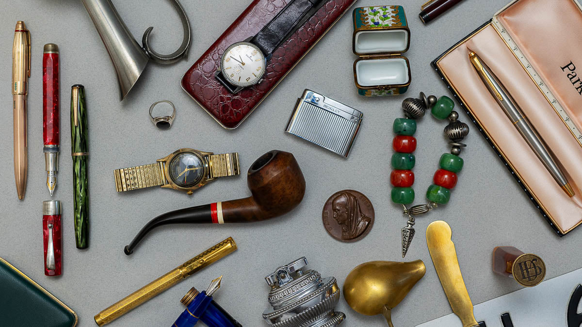 Collection of vintage items including watches, pipes, and jewelry on a gray surface
